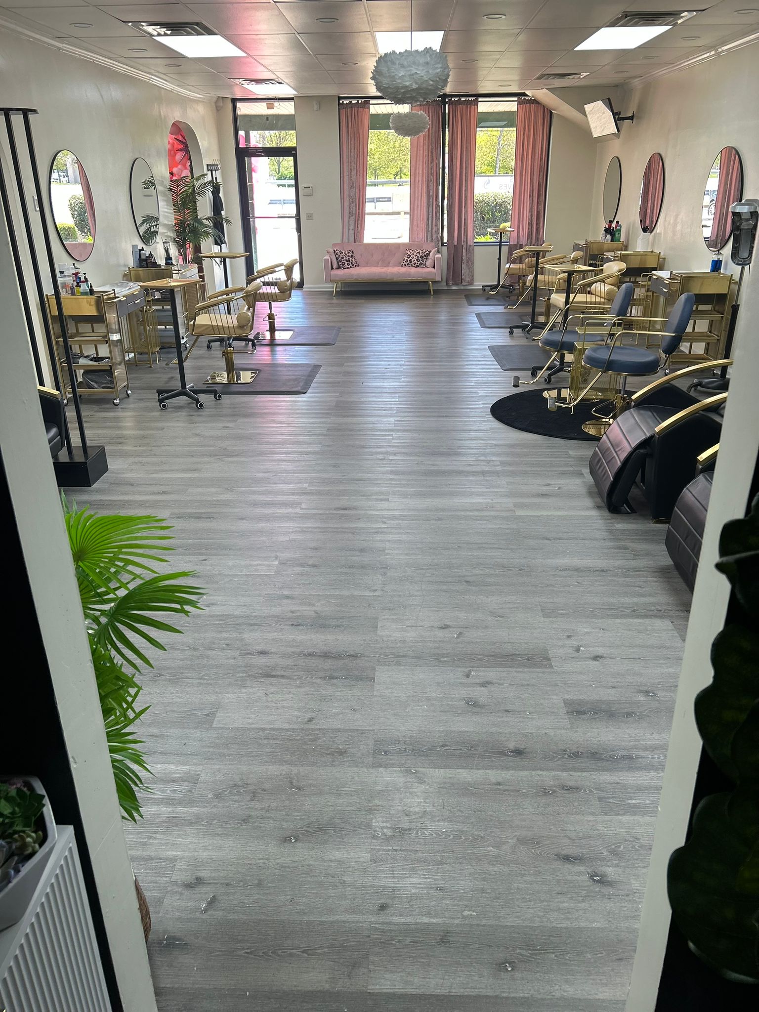 Full salon view from entrance — pink curtains, natural light, all chairs visible